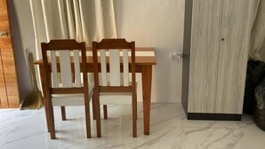 Ein Zimmer mit einem Holzespeisetisch, zwei Stühlen, einem Kleiderschrank und einem an der Wand lehnenden Besen.