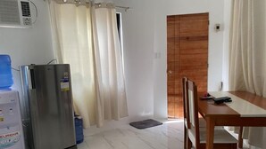 Ein Zimmer mit Holztür, einem Esstisch mit Stühlen, einem Kühlschrank und einem Wasserspender.