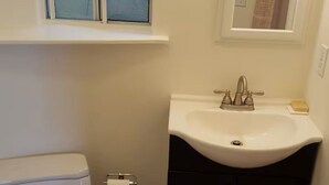 A bathroom with a toilet, sink, and a window with frosted glass. - SC Cozy Beach Apartment (San Clemente)