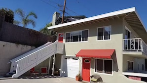 A two-story house with a red front door, a staircase leading to the upper floor, and a balcony with a railing. - SC Cozy Beach Apartment (San Clemente)