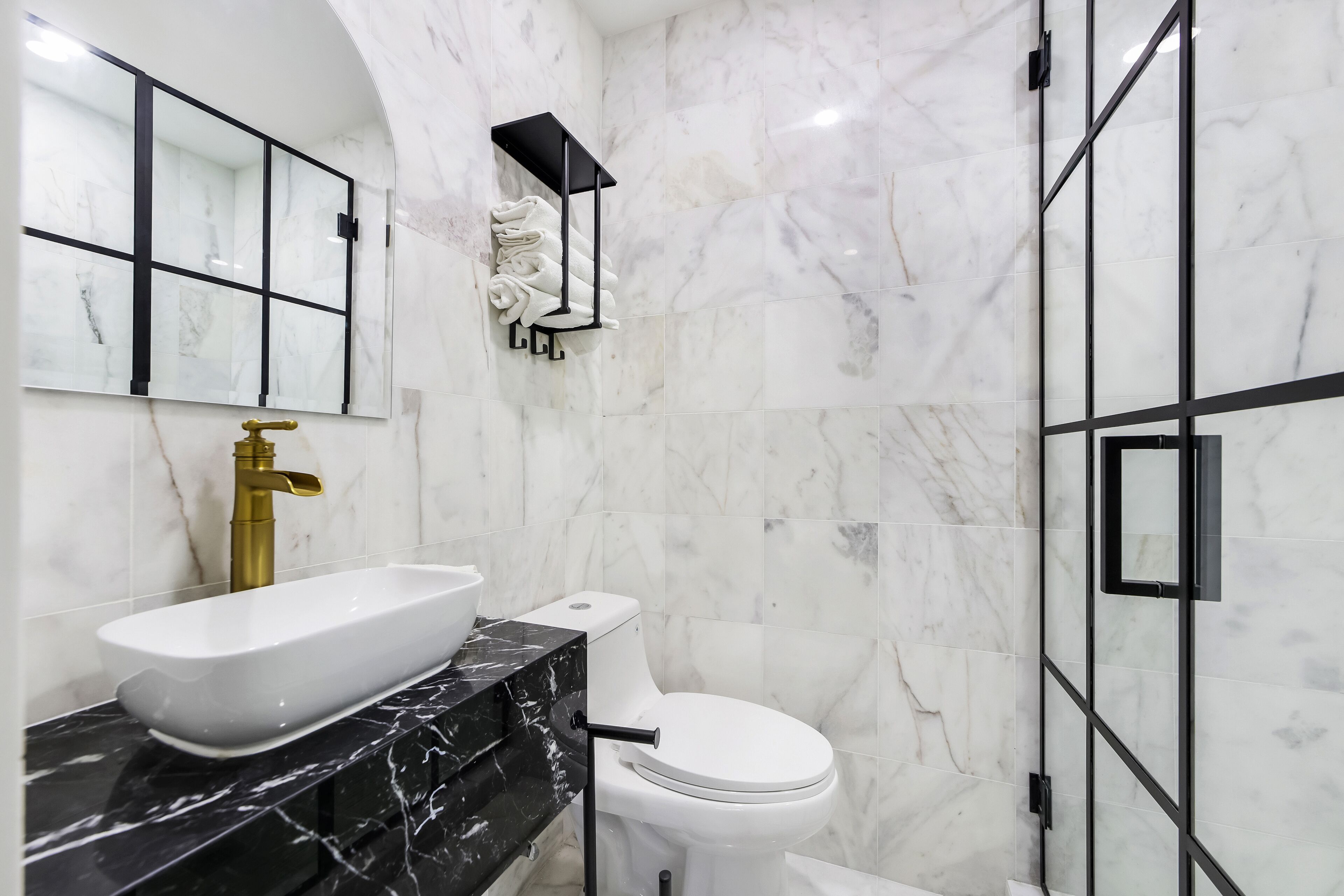Een badkamer met een wit wastafel, een zwart aanrechtblad, een gouden kraan, een wit toilet en een douchecabine van glas.