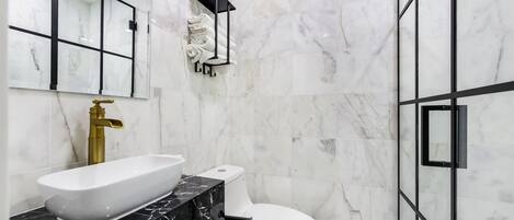 A bathroom with a white sink, black countertop, gold faucet, white toilet, and a glass shower enclosure.