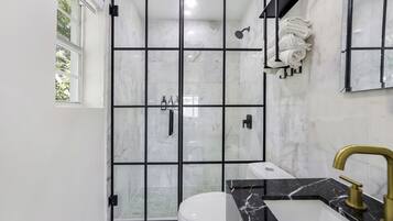 Ein modernes Badezimmer mit Duschkabine aus Glas, einer weißen Toilette, einem schwarzen Marmorwaschbecken und einem goldenen Wasserhahn.