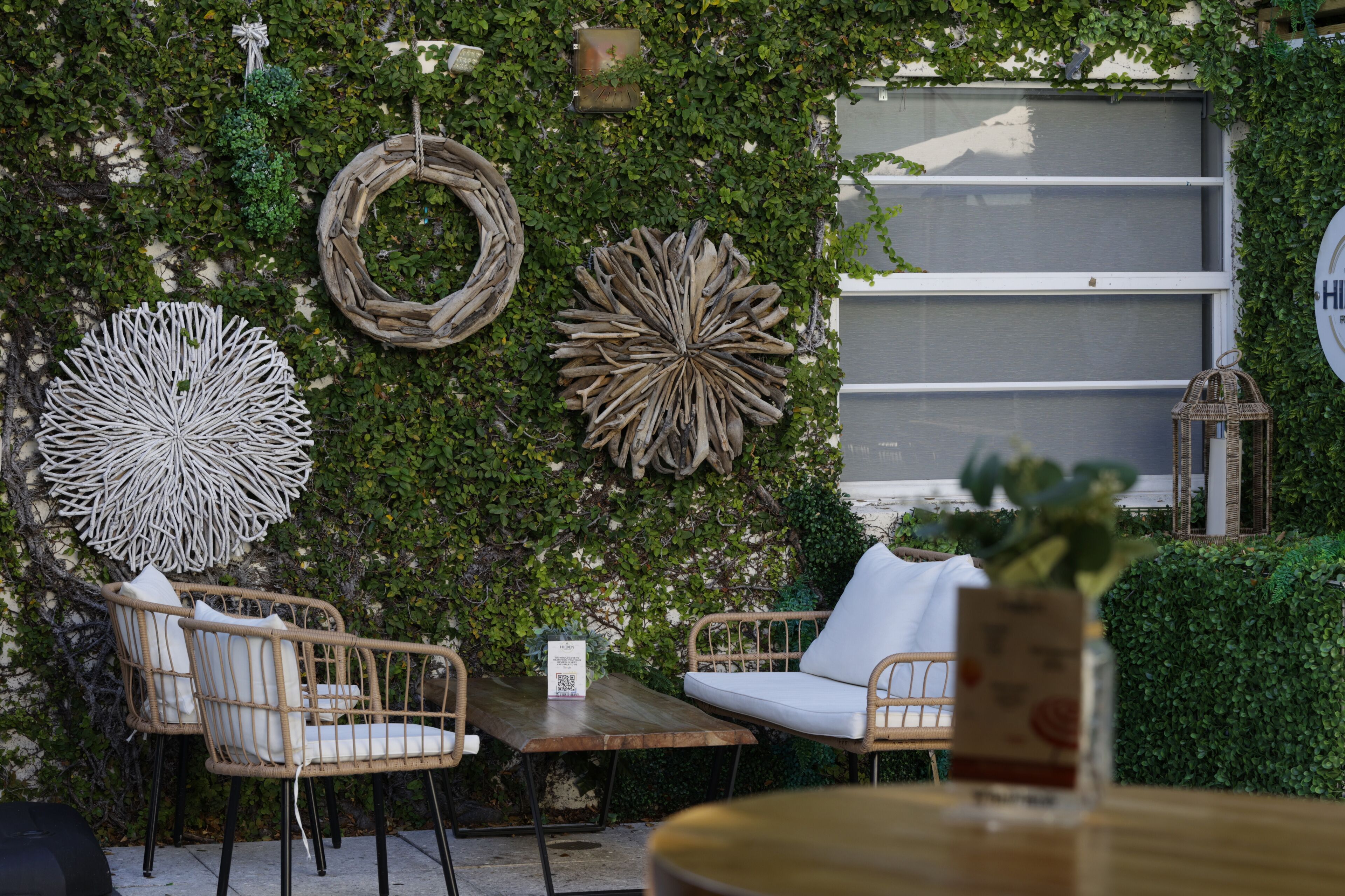 A cozy outdoor seating area with wicker furniture, a wooden table, and decorative wall art.