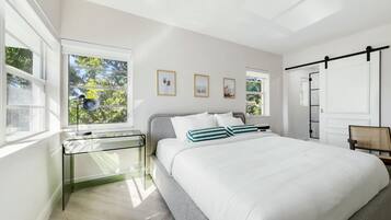 A bedroom with a bed, a glass desk, and a window with a view of trees.