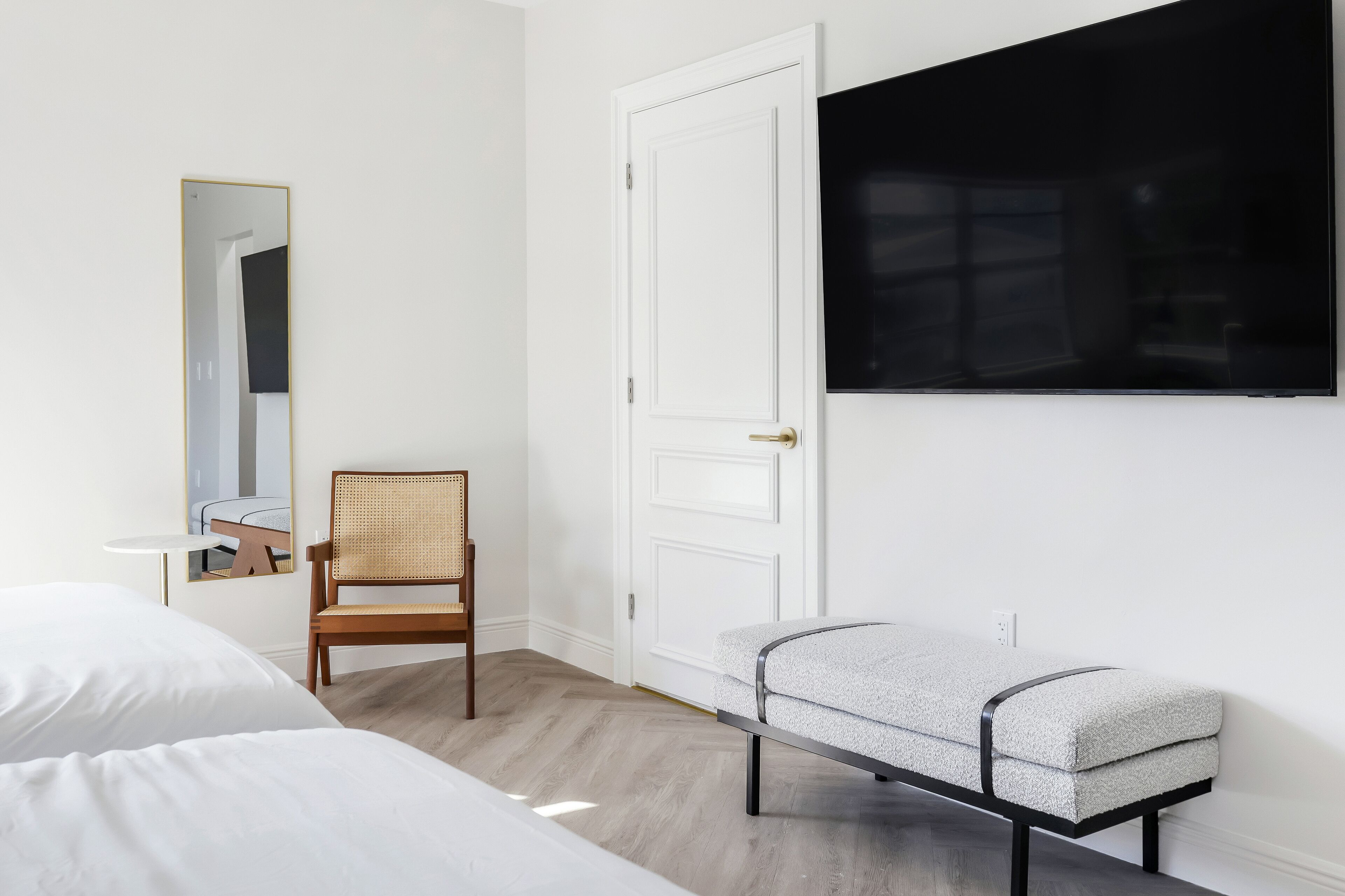 Ein Hotelzimmer mit einem Bett, einem Sessel, einer Bank, einem Spiegel und einer Tür.