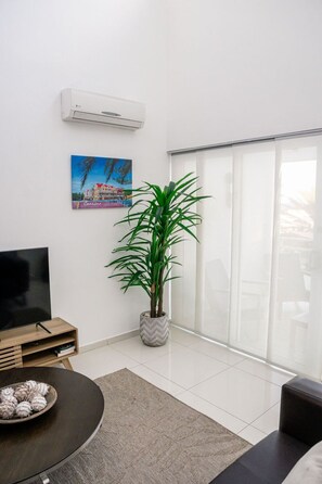 A living room with a flat-screen TV, a potted plant, a painting, and a sliding glass door. - Searenity Penthouse at Piscadera Harbour Village (Willemstad)