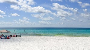 Ein Strand mit weißem Sand, klarem türkisblauem Wasser und ein paar Personen in der Ferne.