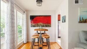 A modern interior with a wooden bar stool set, a red abstract painting, and a view of the outdoors.