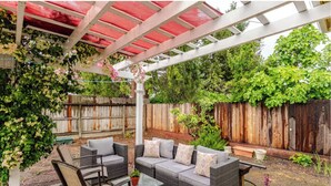 A covered patio with wicker furniture, a pergola, and a wooden fence.