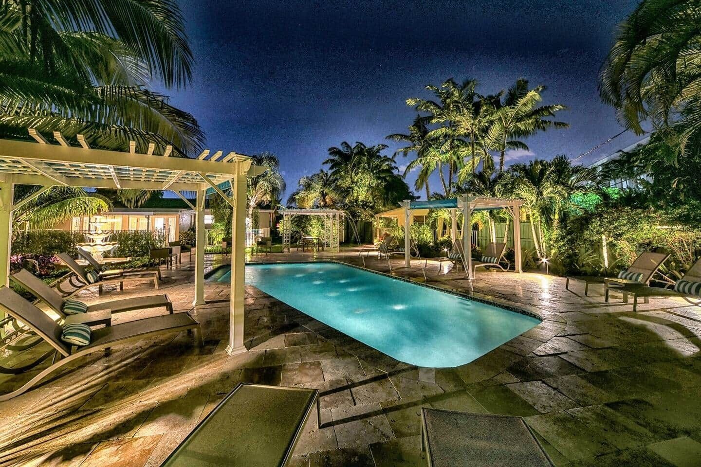 Un espace piscine aménagé pour la nuit, avec des chaises longues et une pergola.