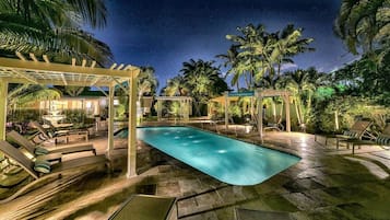 Un espace piscine aménagé pour la nuit, avec des chaises longues et une pergola.