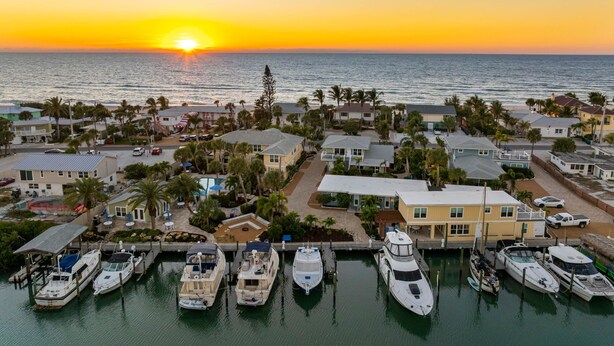 A marina with several boats docked, surrounded by residential buildings and palm trees, with the ocean and sunset in the background. - Hotel Studio (Second Level) - Unit D (Nokomis)