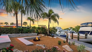 A landscaped outdoor area with a fire pit, palm trees, and boats docked at a marina. - Hotel Studio (Second Level) - Unit D (Nokomis)