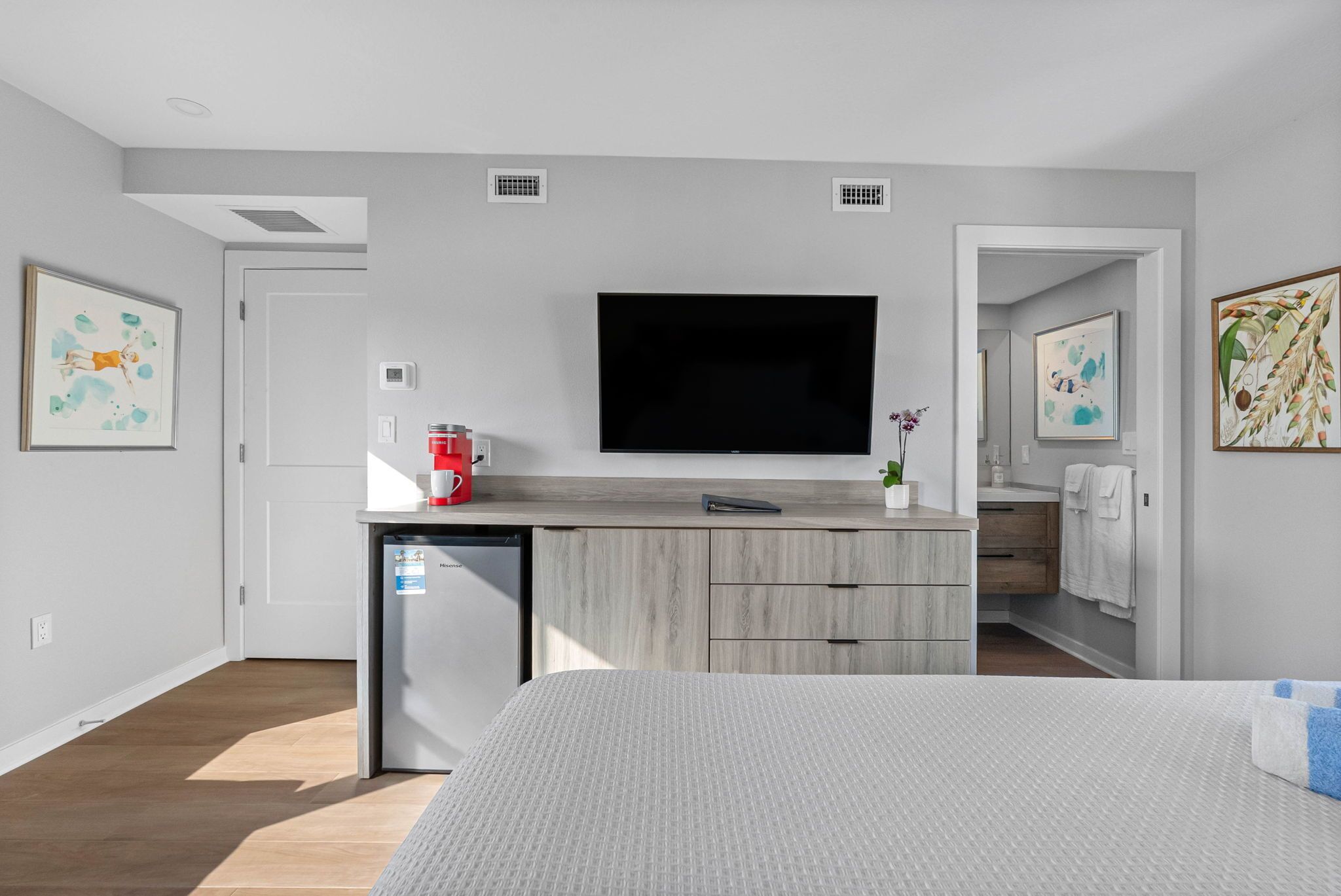Une chambre moderne équipée d’un lit, d’une télévision, d’une petite kitchenette et ornée d’œuvres d’art sur les murs.