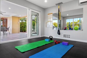 A room with a large sliding glass door leading to an outdoor patio, a ceiling-mounted suspension trainer, and exercise mats.