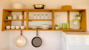 Una cocina con estantes de madera que sostienen tazas blancas, platos y un bol. También hay frascos de vidrio, un recipiente verde y una olla colgante.