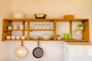 A kitchen with wooden shelves holding white mugs, plates, and a bowl. There are also glass jars, a green container, and a hanging pan. - Hidden Retreat Near Chirripó - Healing, Deep Rest, Inspiration & Mountain Magic (San José Province, Rivas, Costa Rica)