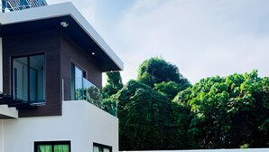 A modern two-story house with a swimming pool, outdoor seating, and lush greenery.