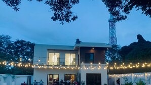 A modern two-story house with a balcony, string lights, and a swimming pool.
