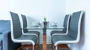 Zona pranzo moderna con un tavolo in vetro, due poltrone rivestite di grigio e un vaso bianco con fiori.