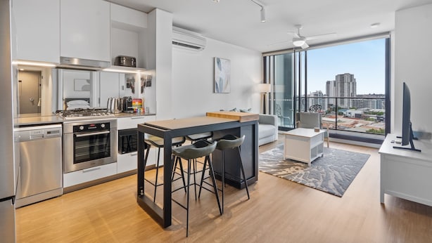 Una cocina moderna con una isla central, electrodomésticos de acero inoxidable y vistas a la ciudad a través de amplios ventanales.