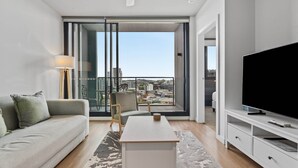 Una sala de estar moderna con un sofá, una mesa de centro, un televisor y vistas de la ciudad a través de amplias ventanas.