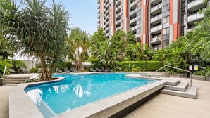 Una piscina con un jardín circundante, escalones que bajan a la piscina y un edificio residencial alto al fondo.