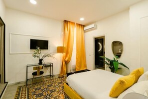 Une chambre d’hôtel avec un lit, un téléviseur fixé au mur, un bureau avec une chaise et une plante en pot.