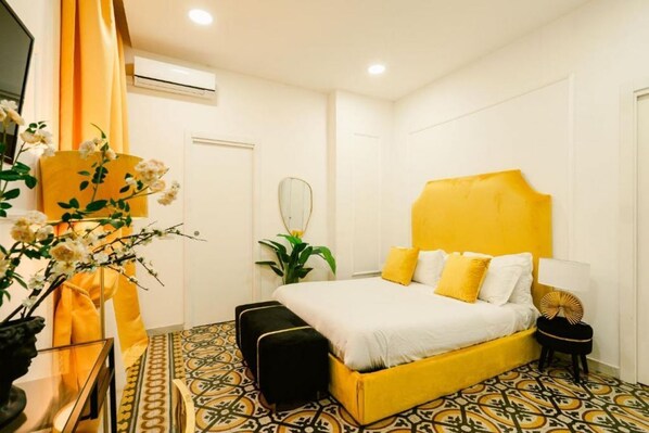 Une chambre avec un lit jaune, des oreillers blancs et un sol à motifs.