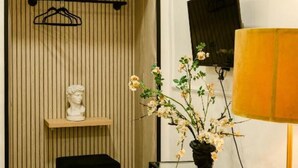 A room with a wooden slat wall, a white bust sculpture, a black sofa, a vase with flowers, and a wall-mounted TV. - Random Superior  By Dimorra (Naples)