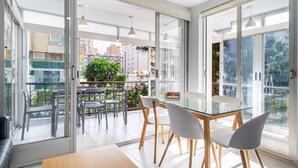 Un comedor moderno con una mesa y sillas de vidrio, ventanas amplias y vistas a la ciudad.