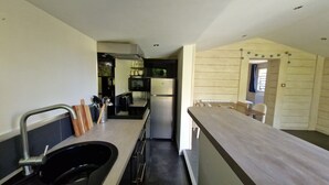 Une cuisine compacte équipée d’un évier, d’une cuisinière et d’un réfrigérateur. Un coin repas est aménagé avec une table et des chaises.