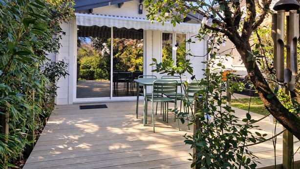 Un espace extérieur aménagé en patio, doté d’un coin salon couvert, d’une terrasse en bois et entouré de verdure.