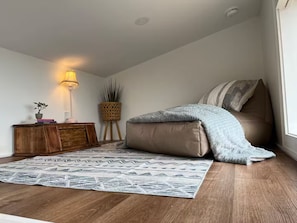 Ein Schlafzimmer mit einem Bett, einem Nachttisch, einer Lampe, einer Pflanze und einem gemusterten Teppich.