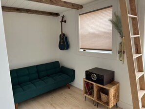 Ein gemütliches Zimmer mit einem grünen Sofa, einer Gitarre, einem Radio und einem Fenster mit Jalousien.