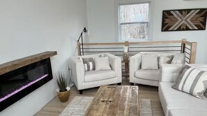 Un salon doté d’une cheminée, de deux canapés blancs, d’une table basse et d’une fenêtre donnant sur des arbres.