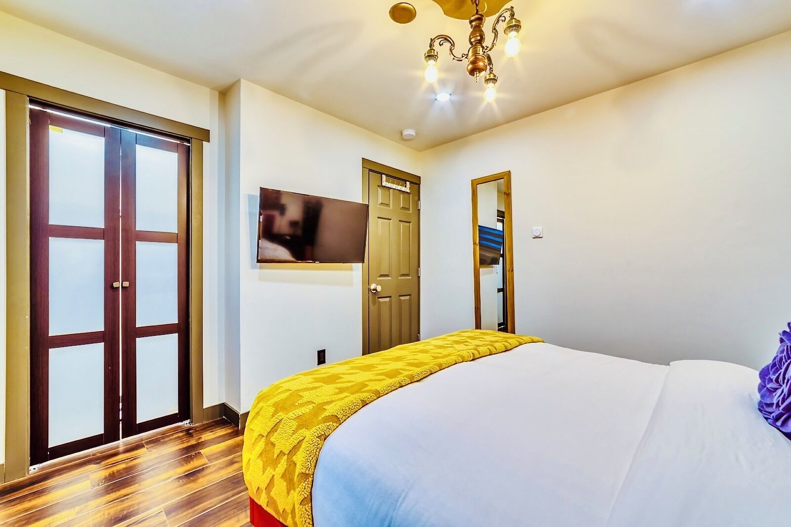 A hotel room with a large bed, a television mounted on the wall, and a wooden floor.