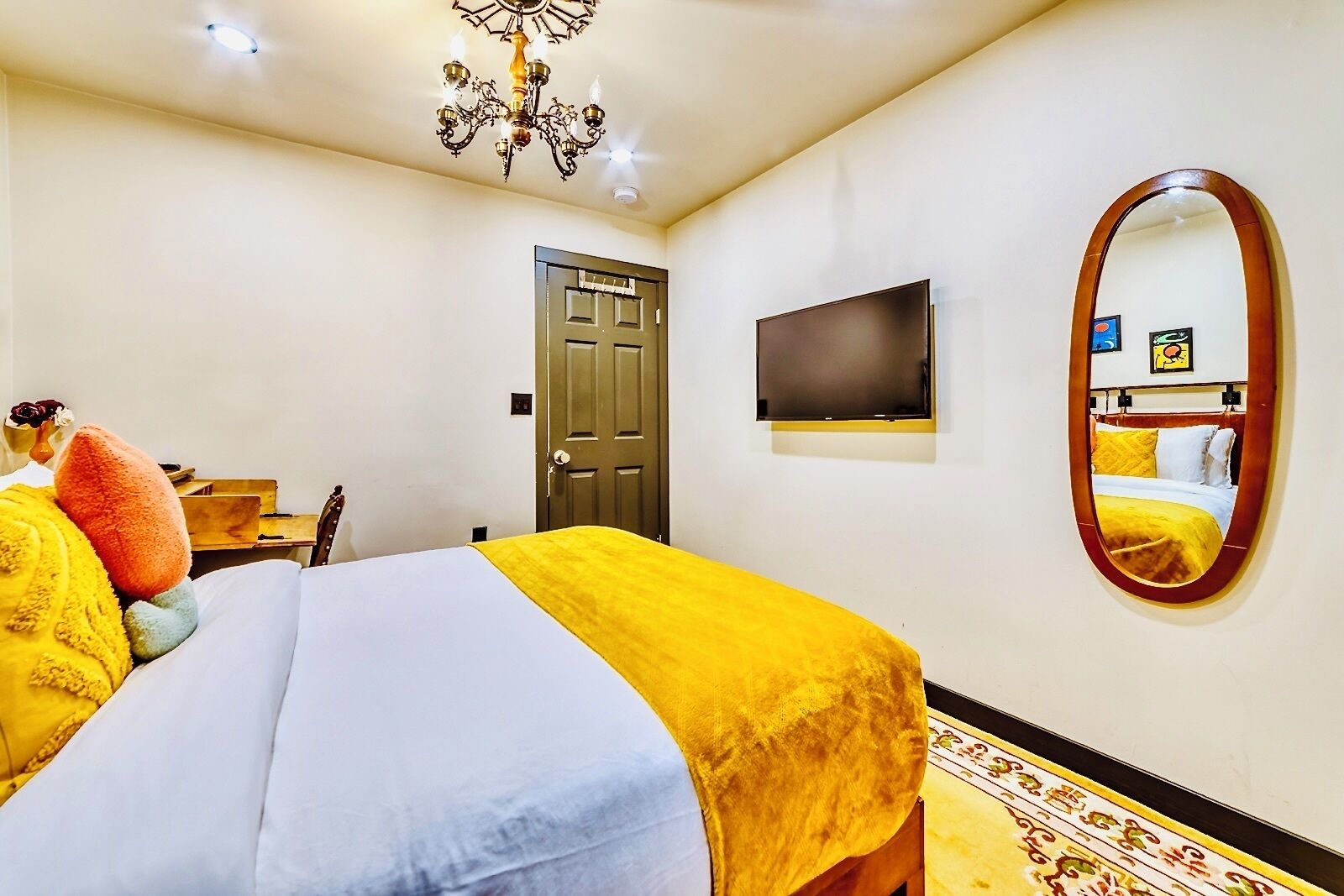 A hotel room with a bed, a television, a door, and a mirror.