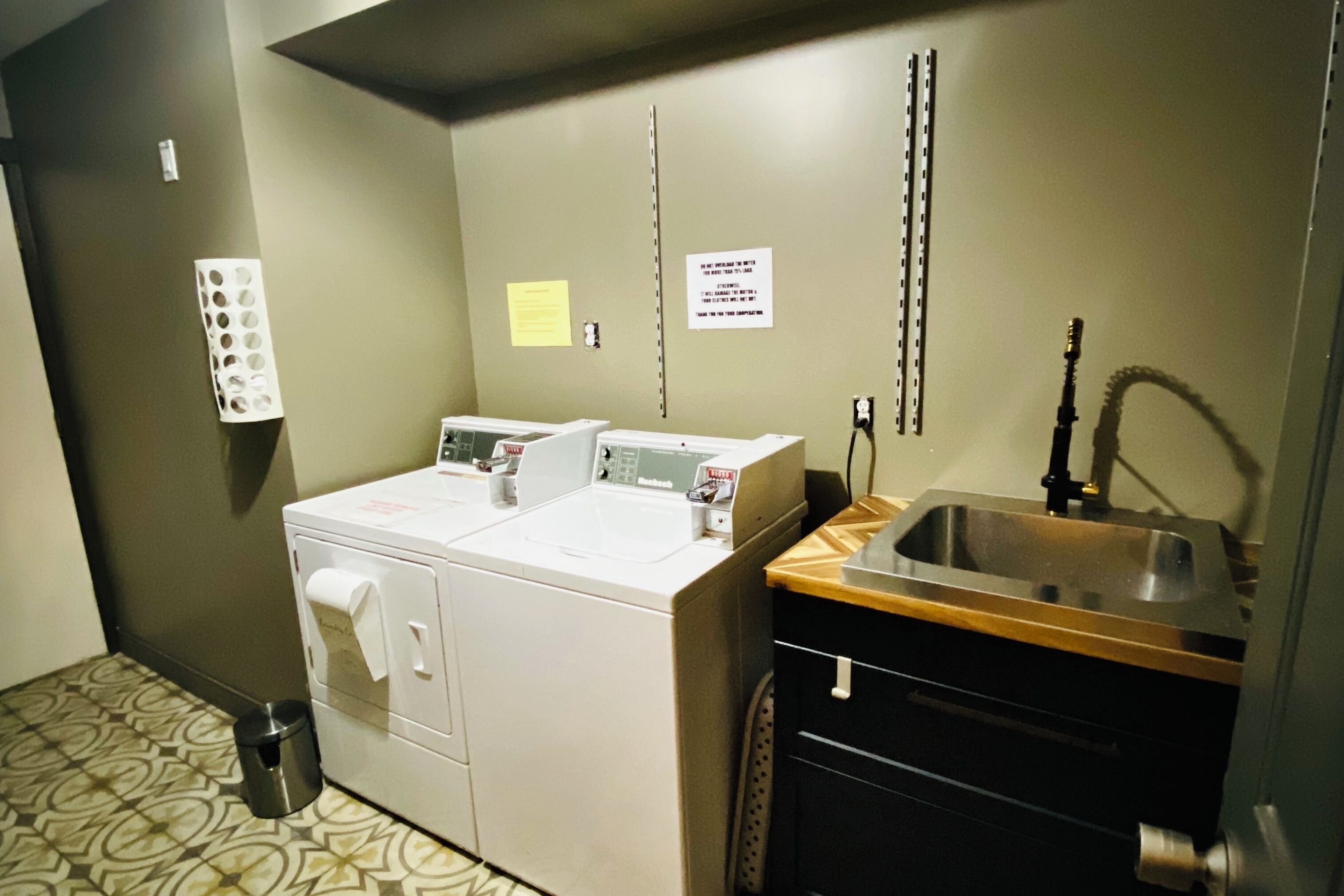 A laundry area with a washing machine, dryer, sink, and a trash can.