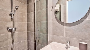 Een badkamer met een douche, wastafel en een ronde spiegel.