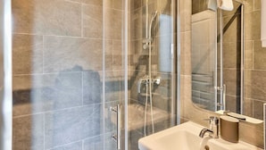 Een moderne badkamer met een douchecabine van glas, een witte wastafel en een grote spiegel.