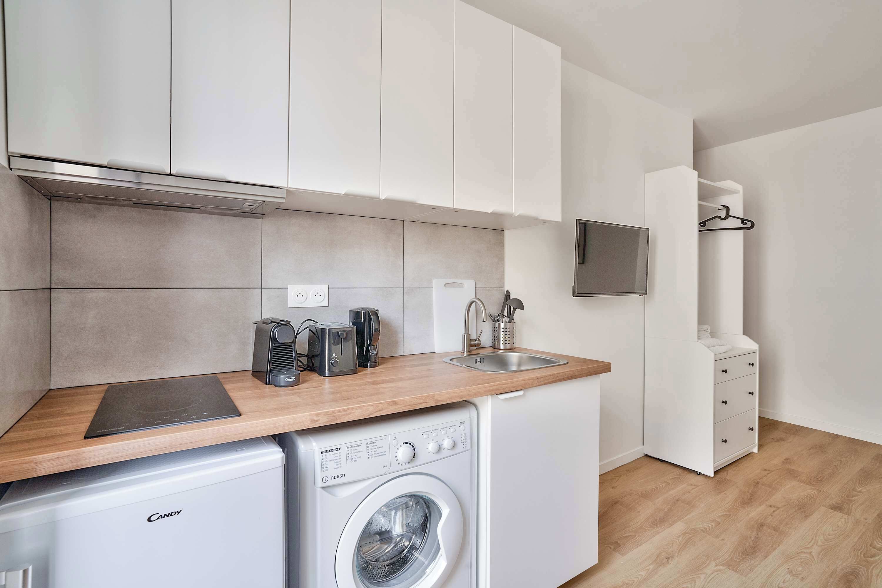 A compact kitchen with a washing machine, a coffee maker, and a toaster.