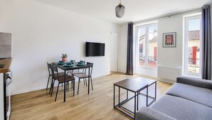 Un soggiorno moderno con un divano grigio, un tavolo da pranzo con sedie, una televisione a schermo piatto e un'ampia finestra con tende.