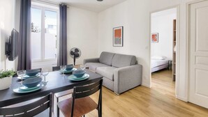 Un soggiorno moderno con zona pranzo, un divano grigio e un letto sullo sfondo.