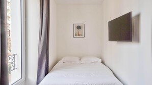 Quarto com cama, janela com cortinas, quadro na parede e televisão de tela plana presa à parede.
