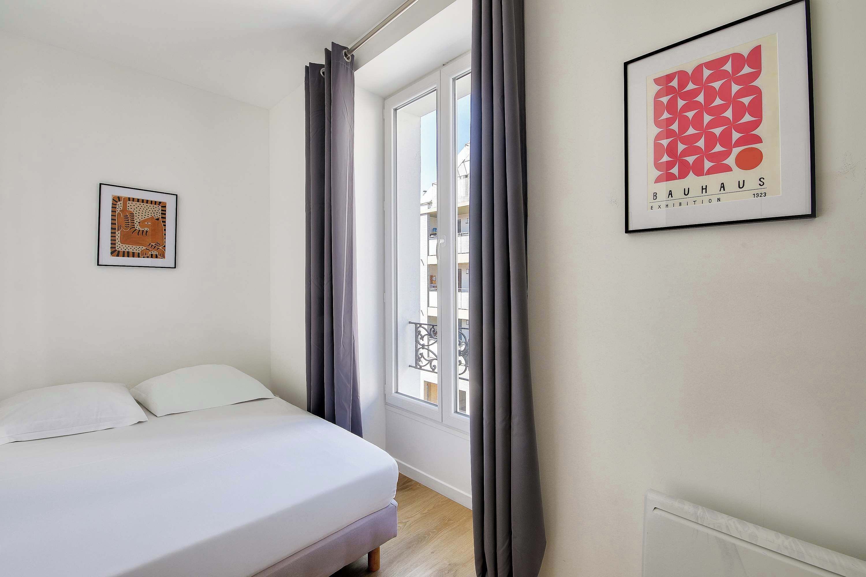A bedroom with a bed, a framed abstract art piece, and a window with curtains.