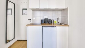 A compact kitchen with white cabinets, a built-in dishwasher, and a countertop with a kettle and coffee maker. - Beautifully furnished cosy studio with a street view (Ivry-sur-Seine)