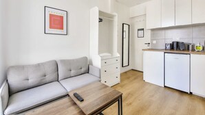 A modern living space with a grey sofa, a wooden coffee table, a small kitchen area with a fridge, and a framed artwork on the wall. - Beautifully furnished cosy studio with a street view (Ivry-sur-Seine)