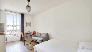 A hotel room with a bed, a desk with a chair, a sofa, and a window with curtains. - Beautifully furnished cosy studio with a street view (Ivry-sur-Seine)